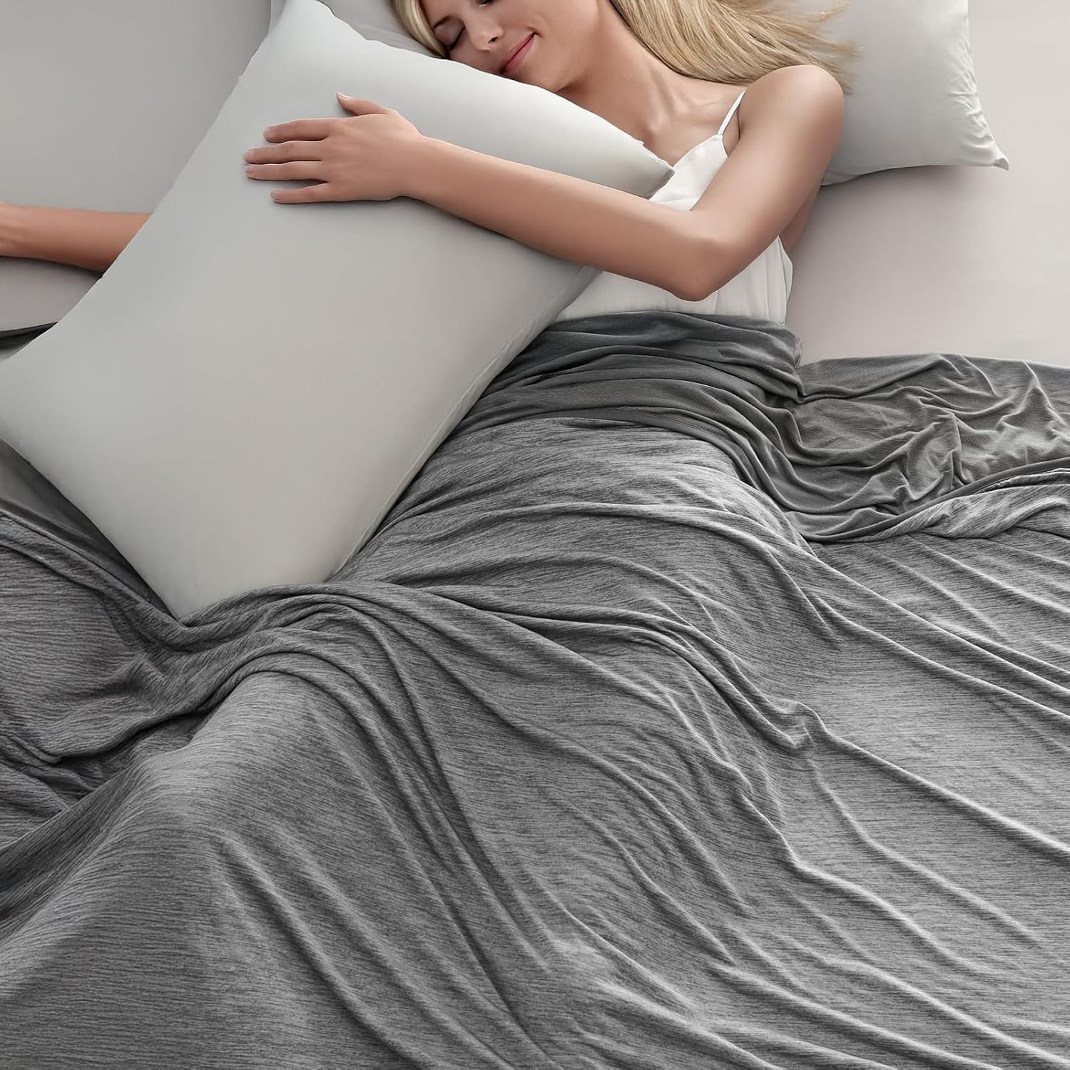 The Arc-Chill cooling blanket in Grey spread across a bed, with a woman asleep under it